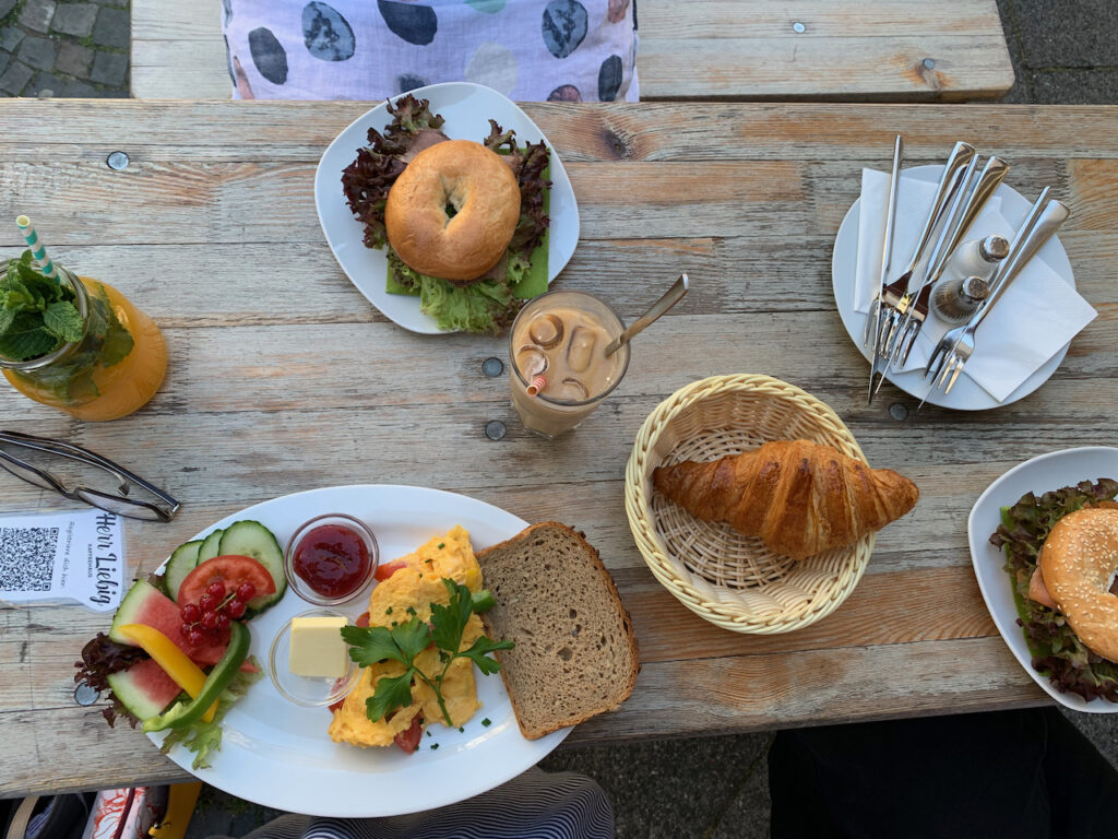 Frühstück bei Herrn Liebig: Tisch mit Bagels, Rührei, Croissant und Getränken