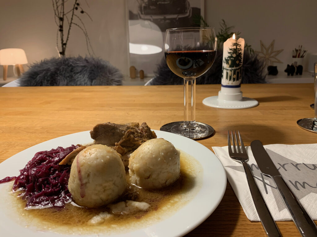 Weihnachtsessen mit Gans, Rotkohl und Klössen. Dazu ein Glas Wein und eine Weihnachtskerze