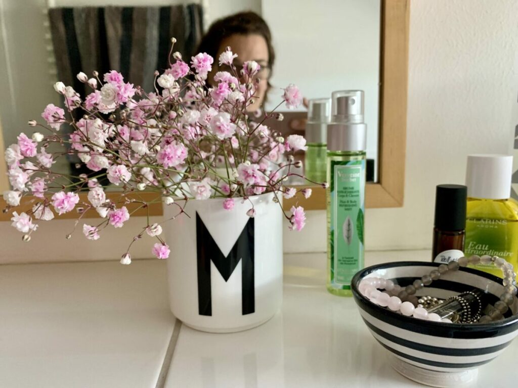 Weiße Tasse mit rosé-farbenem Schleierkraut vor Spiegel im Bad