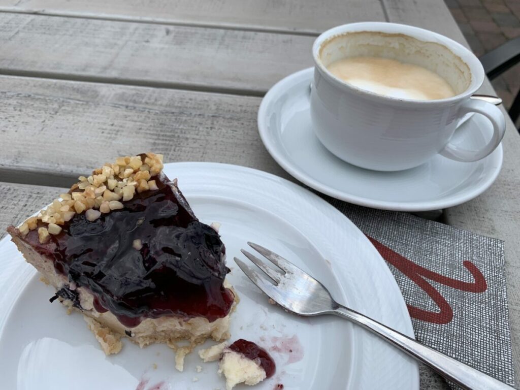 Kaffee und Kuchen: Halb-aufgegessenes Stück Blaubeerkuchen und eine halb geleerte Tasse Milchkaffee