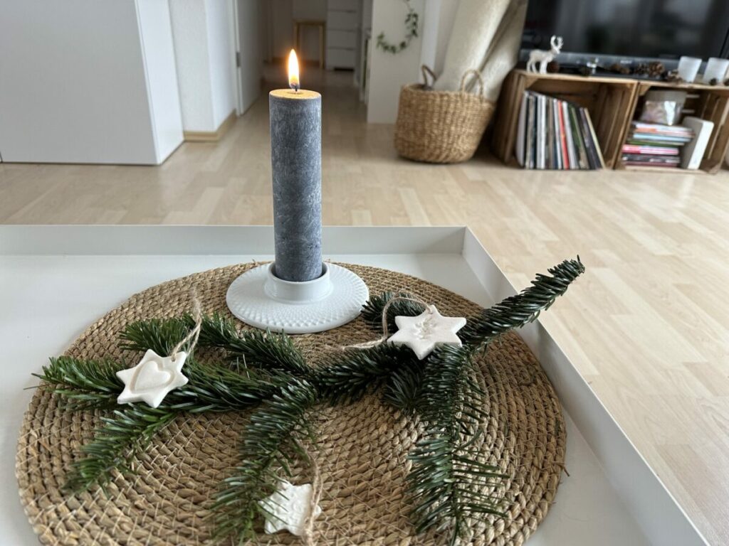 Brennende Allgäuer Heilkräuterkerze "Rauhnächte" auf einer Bastmatte mit Tannenzweig und Tonsternen