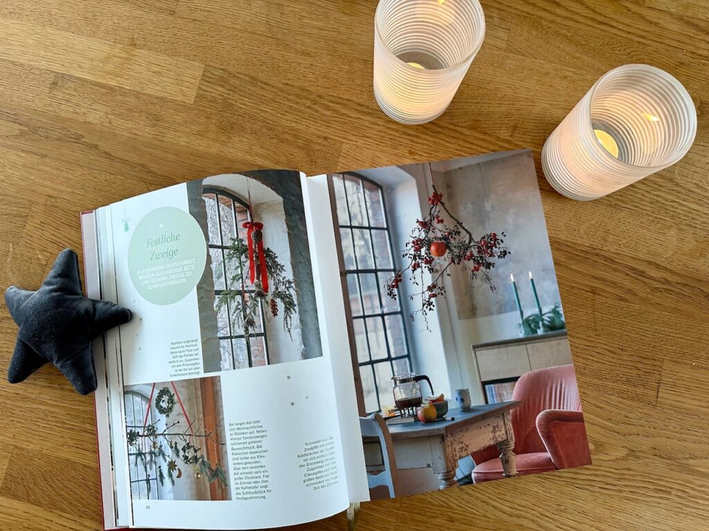 Aufgeschlagene Seite im Landlust Weihnachtsbuch: Abbildungen von Zweigen, die zur Dekoration ins Fenster gehängt werden