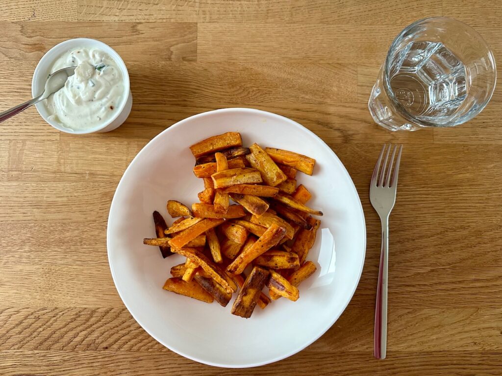 Süßkartoffel-Pommes fertig angerichtet auf dem Teller mit Schnittlauch-Dip in einem Schälchen daneben.