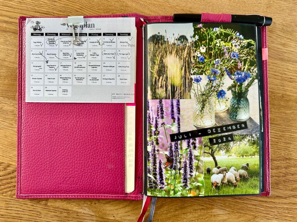 Kalenderhülle aus pinkfarbenem Leder geöffnet: Auf der linken Seite sehen wir den ausgedruckten Yoga-Monatsplan von Mady Morrison mit einer Klammer befestigt. Rechts ein Kalenderheft mit Deckblatt, das mit einer NaturbilderCollage versehen ist und den Titel trägt "Juli - Dezmber 2024" 
