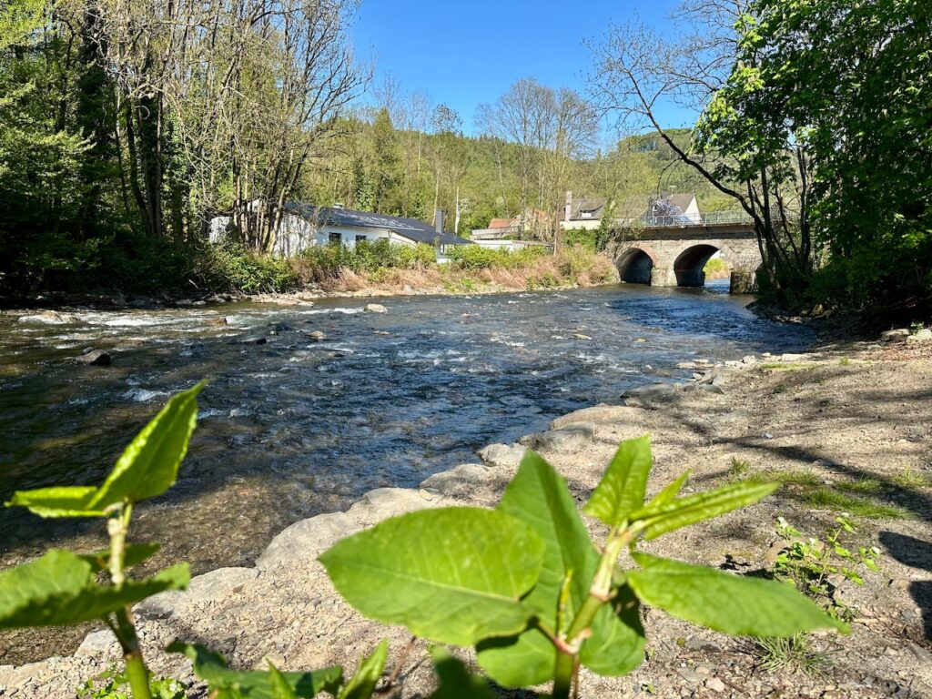 Blick auf die Volme bei Hagen-Dahl: Ein stieniges Flussufer und im Hintergrund eine steinerne Brücke mit Rundbögen