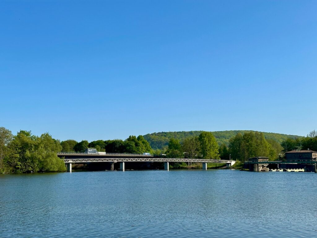 Volmemündung in Hagen, von der Herdecker Ruhr-Seite aus fotografiert. Man sieht die Ruhr, rechts ein Stück vom Staudamm und mittig mündet die Volme in die Ruhr, darüber zwei Brücken: Eine Autobahnbrücke und eine Brücke für Fußgänger und Fahrräder. 