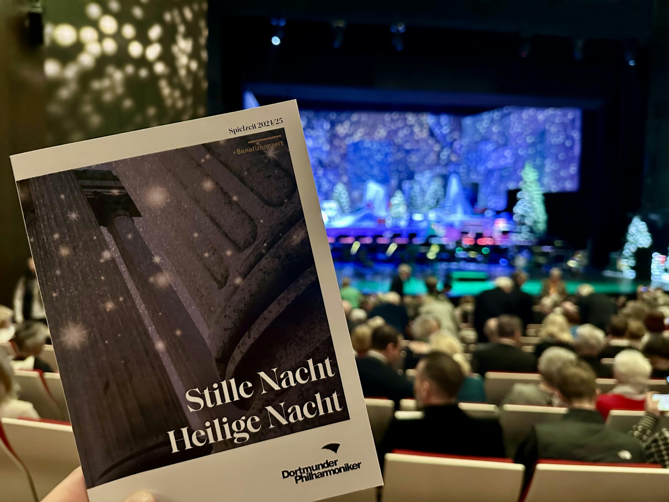 Programmheft vom Konzert "Stille Nacht, Heilige Nacht" der Dortmunder Philharmoniker. Im Hintergrund sieht man das Publikum und die Bühne vor Vorstellungsbeginn.