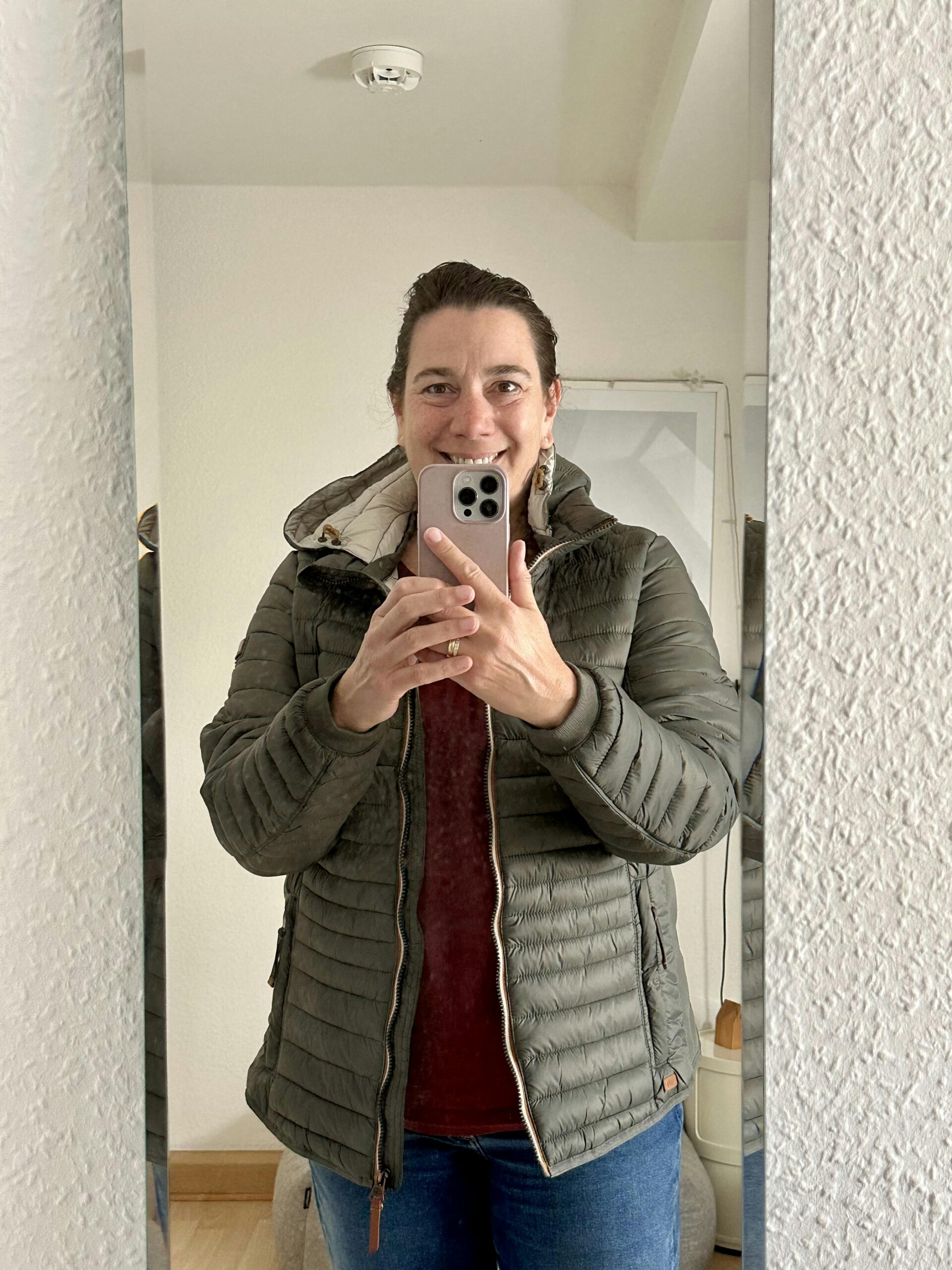 Frau in khaki-farbener Steppjacke vor dem Spiegel
