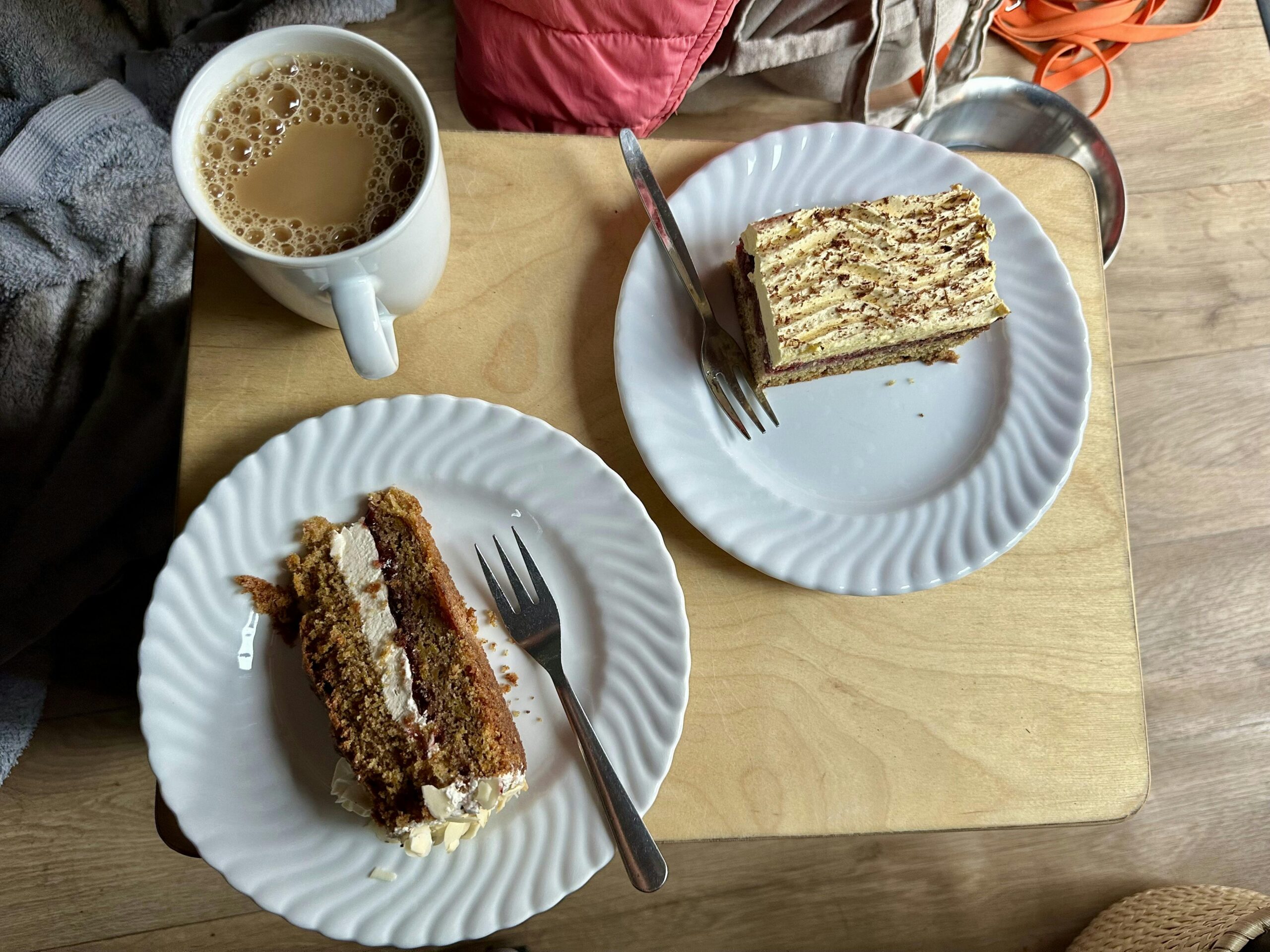 Zwei Teller mit Kuchen sowie eine Tasse Milchkaffee auf einer Kiste mit Holzbrett.