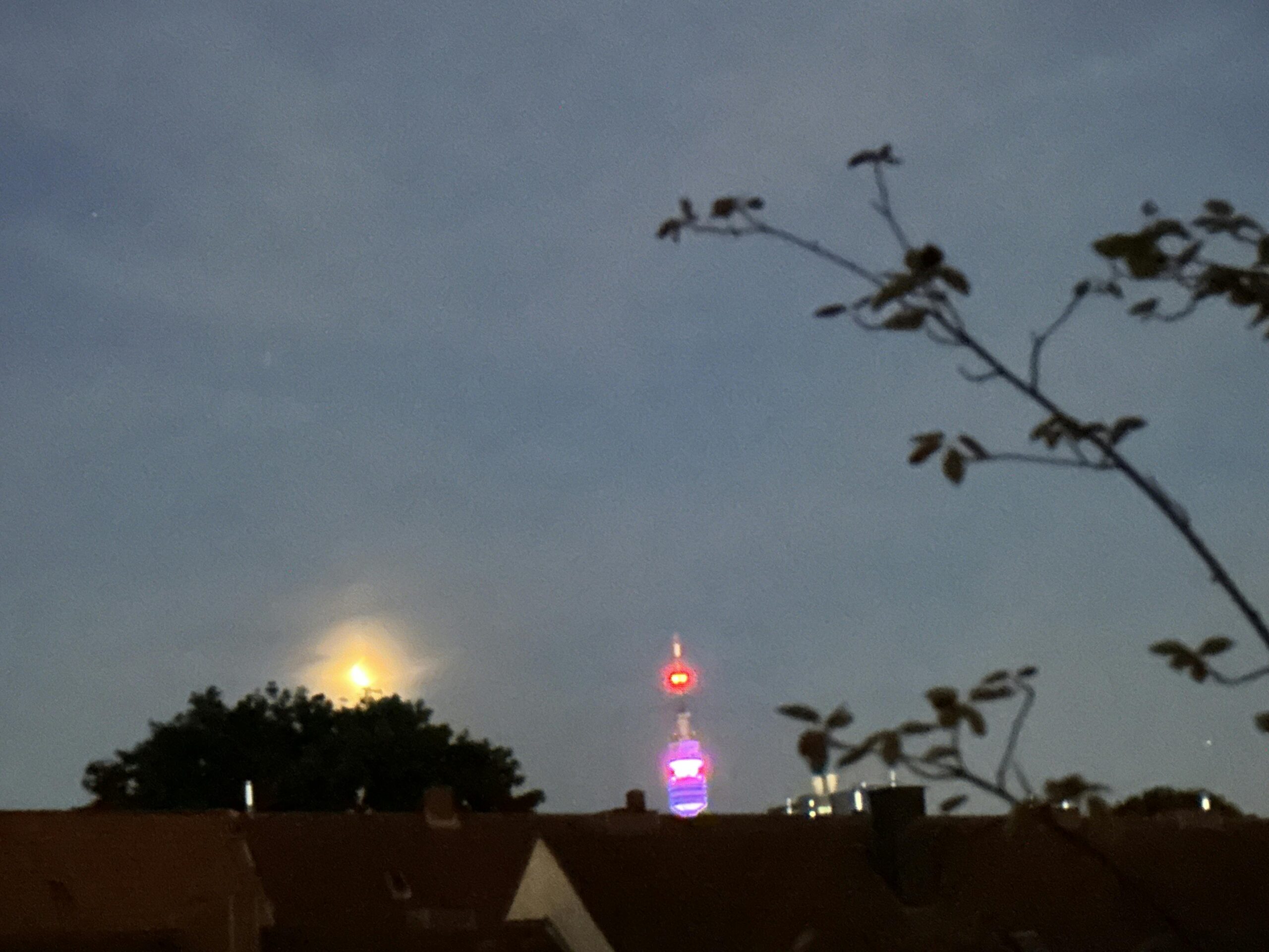Foto vom Mond über den Dächern der Stadt. Der Mond steht über einem Baum, daneben sieht man die Spitze vom Florianturm in Dortmund.