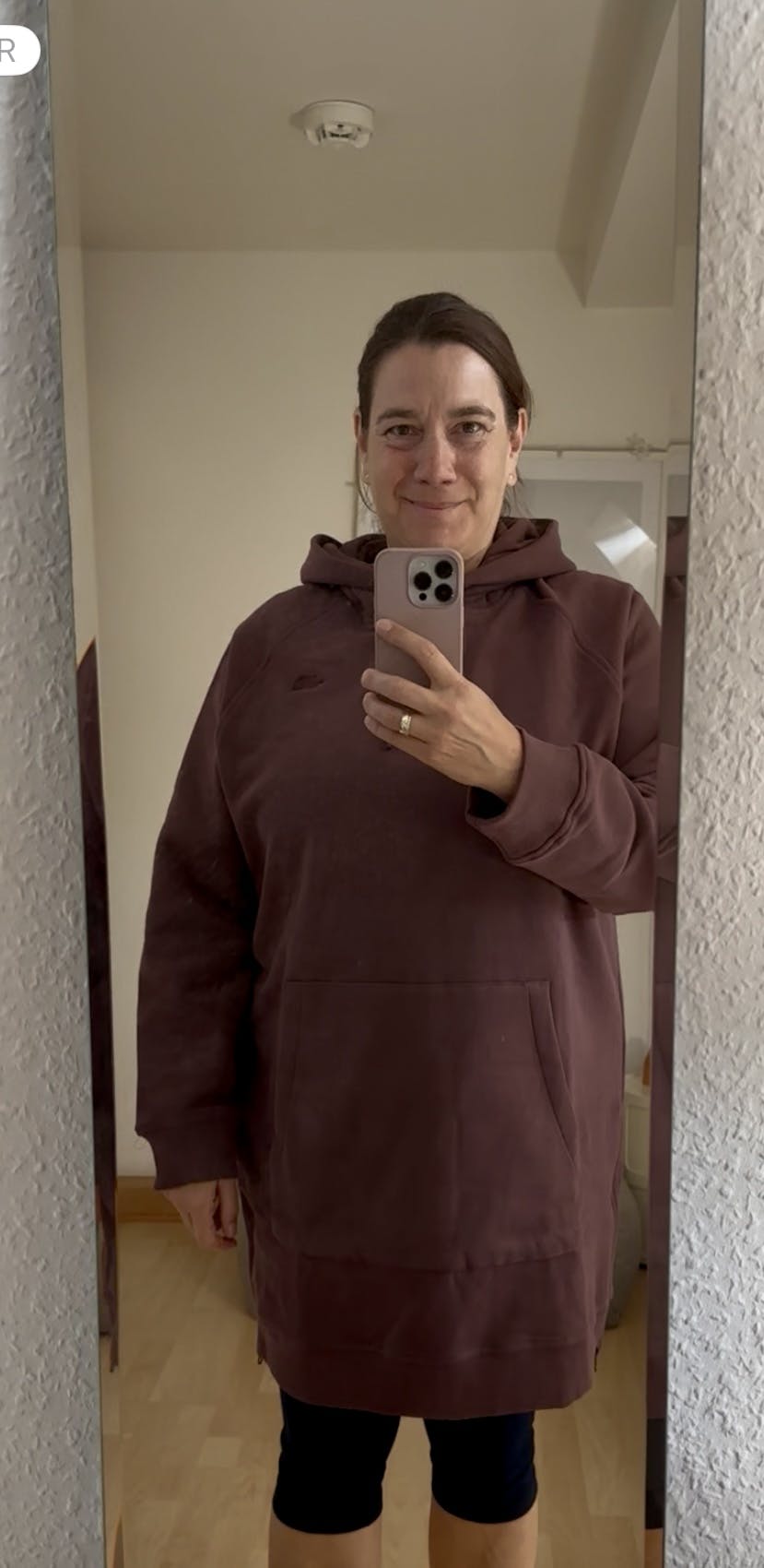 Frau beim Aufnehmen eines Selbstportraits im Spiegel mit dunkelrotem Hoodiekleid und Leggings