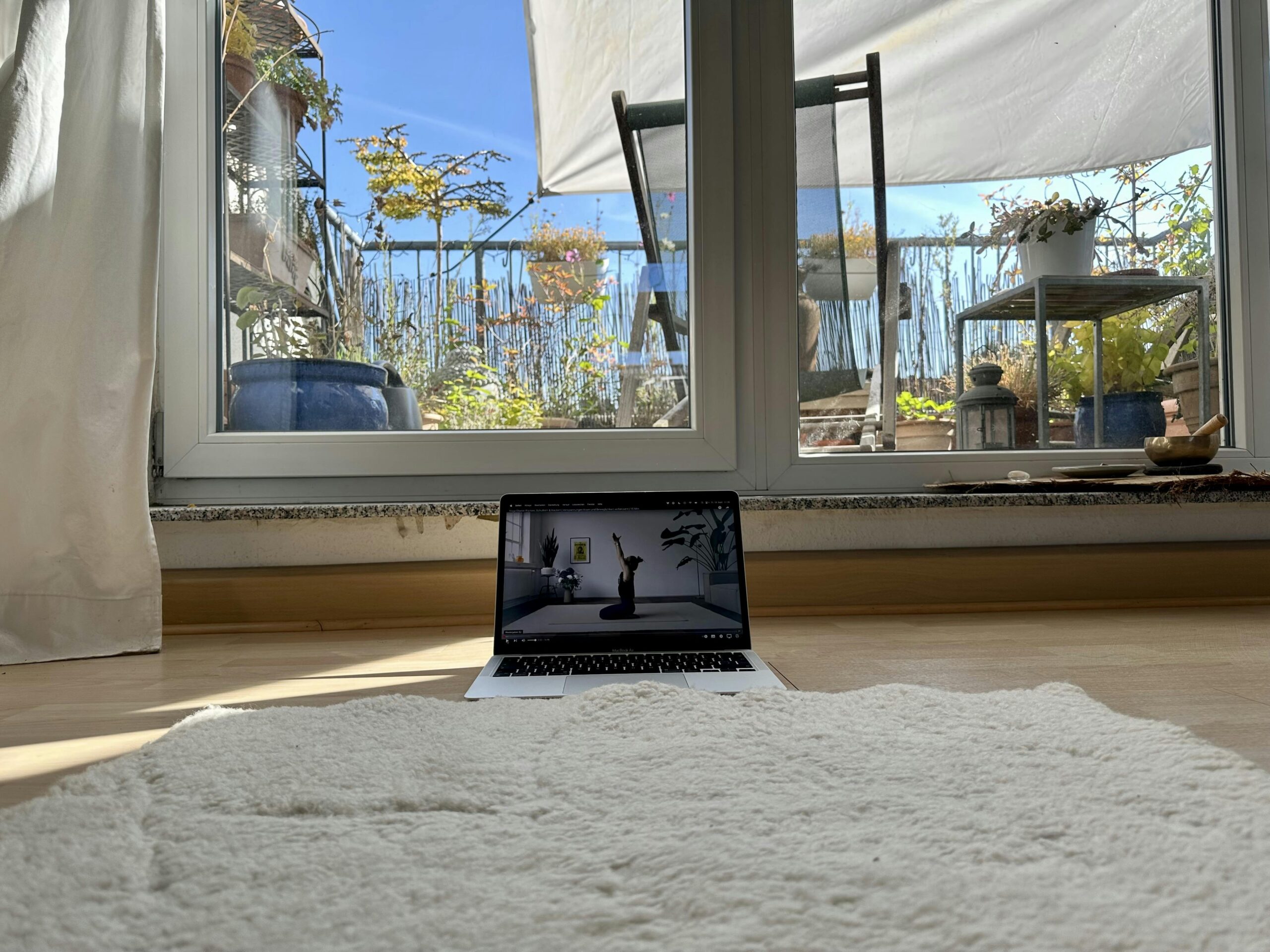 Yogamatte aus Schurwolle vor einem Laptop auf dem eine Frau zu sehen ist, die Yoga macht.