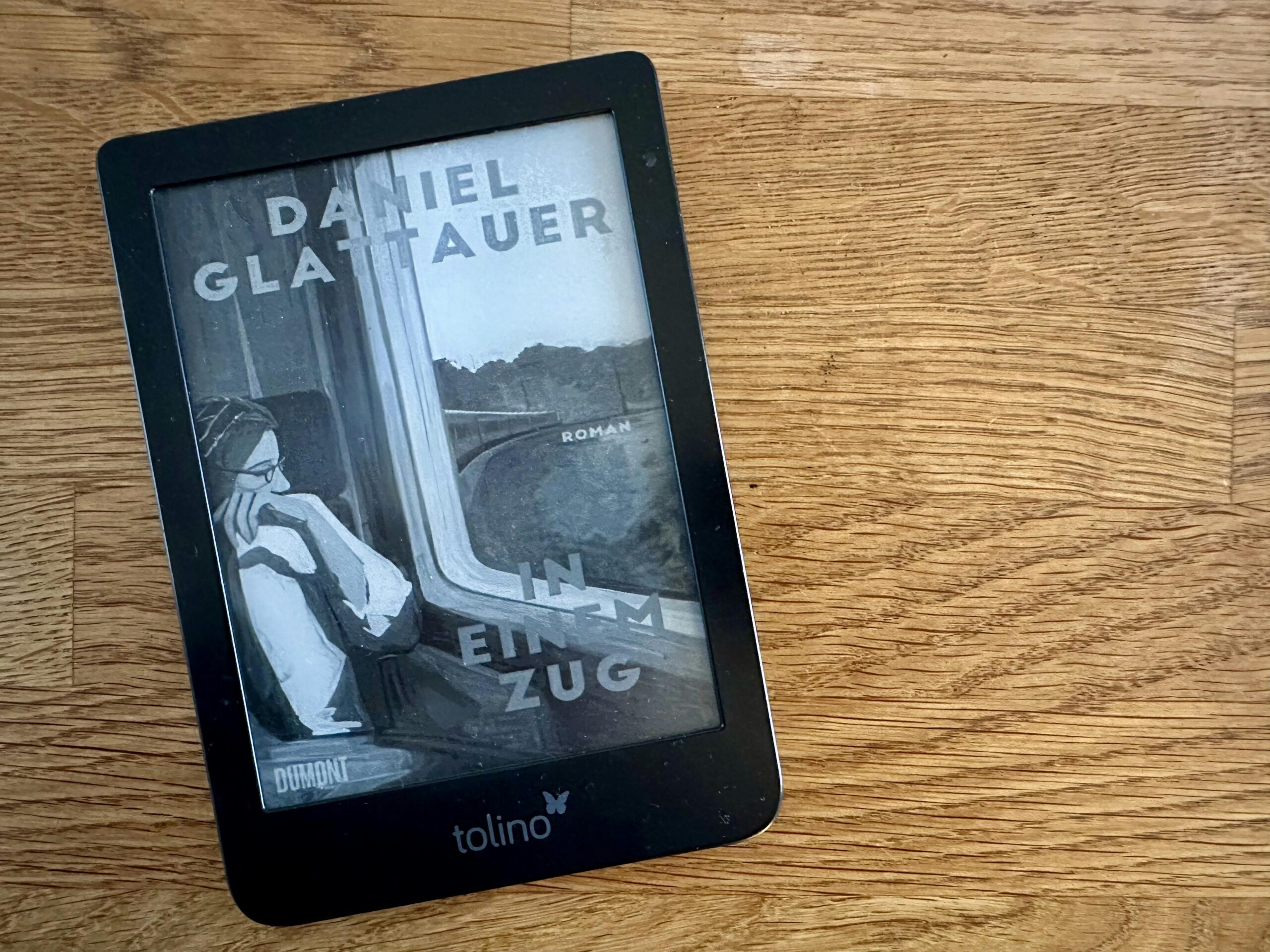 eReader auf einem Holztisch mit dem Titelbild von "In einem Zug" von Daniel Glattauer.