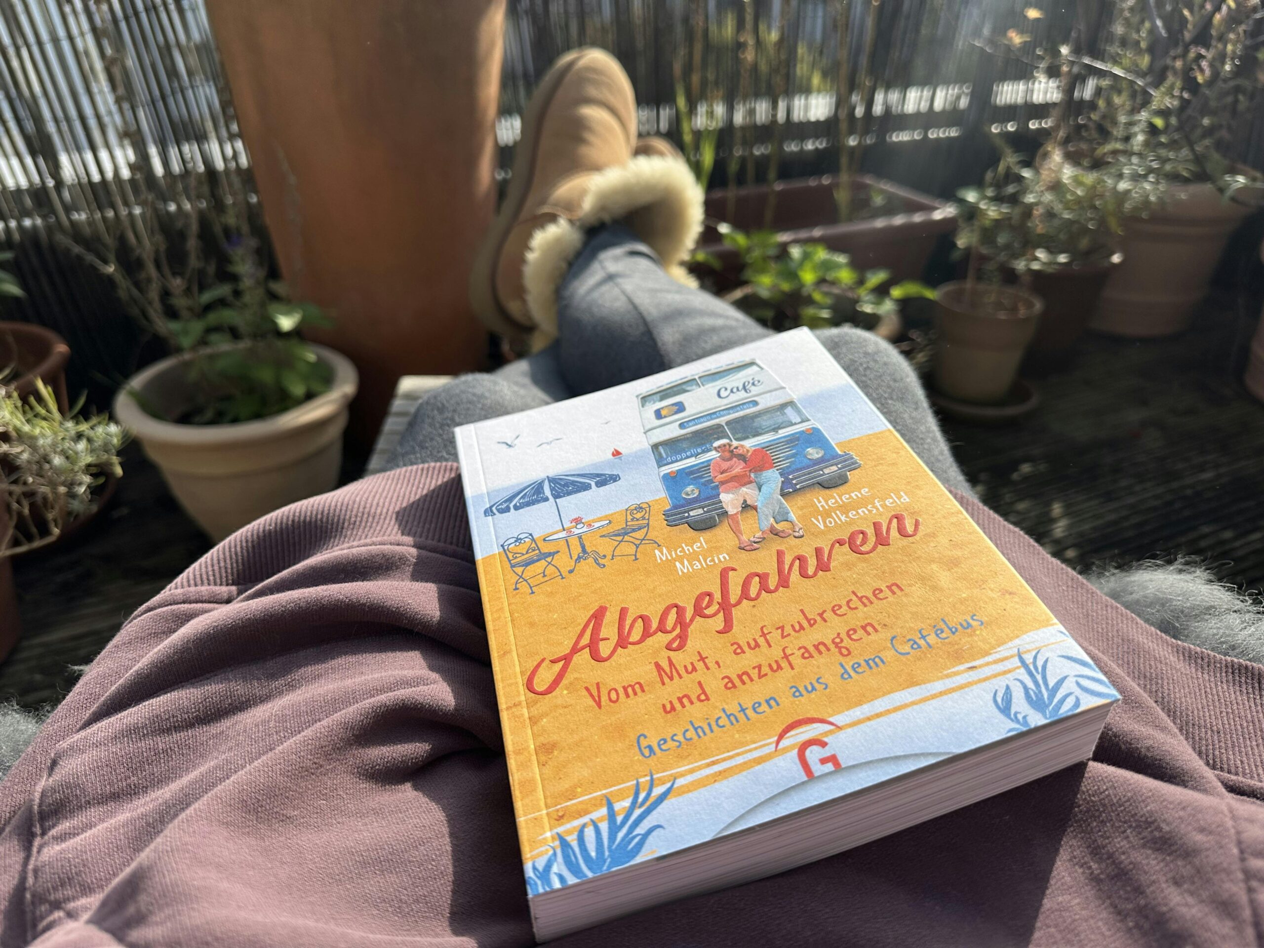 Das Buch "Abgefahren" von Michel Malcin und Helene Volkensfeld auf dem Schoß einer Frau, die bei Sonnenschein draussen liegt.