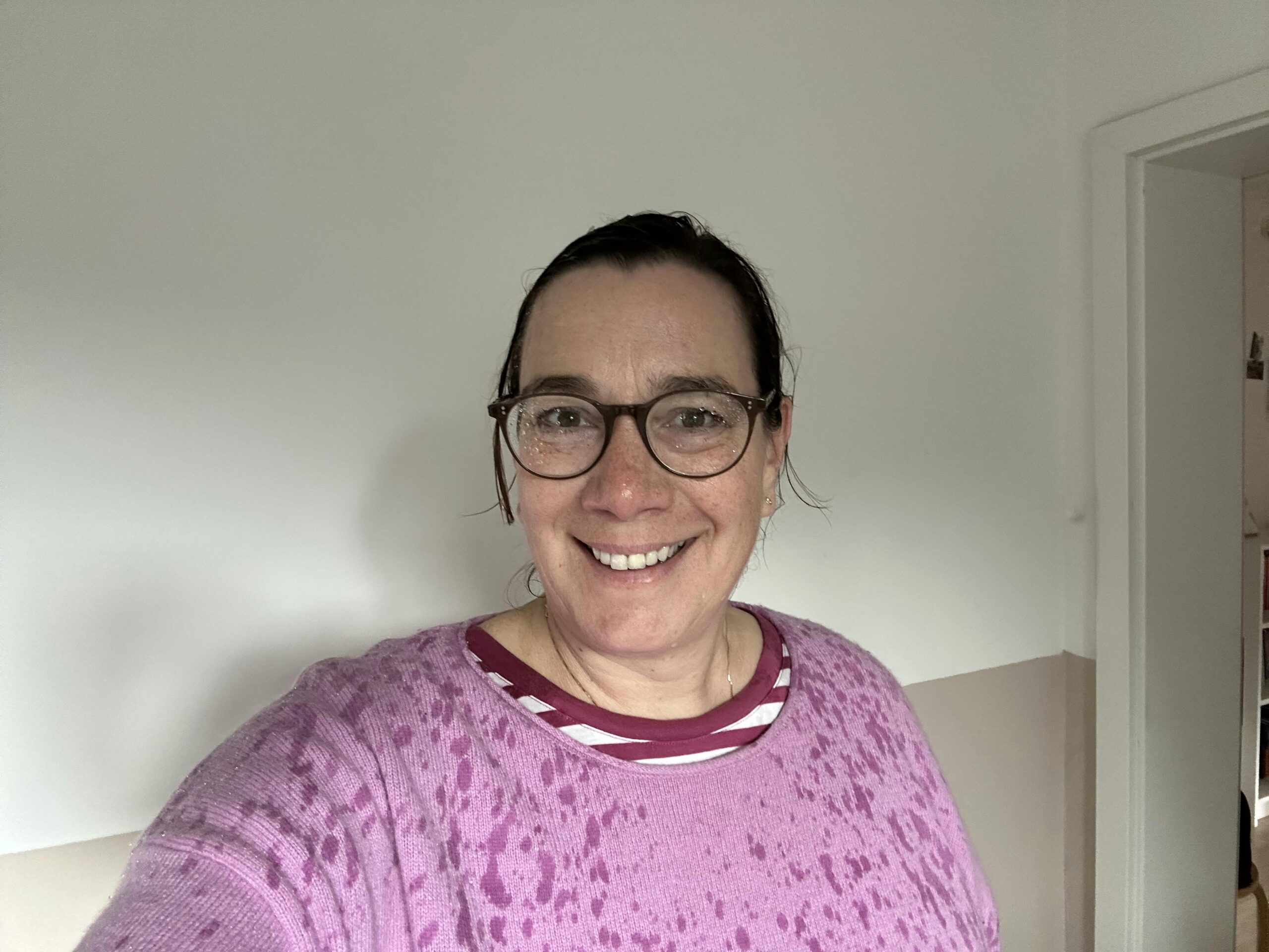 Frau nach Regenschauer mit nassen Haaren, nasser Brille und nassen Flecken auf dem pink-farbenen Strickpullover.