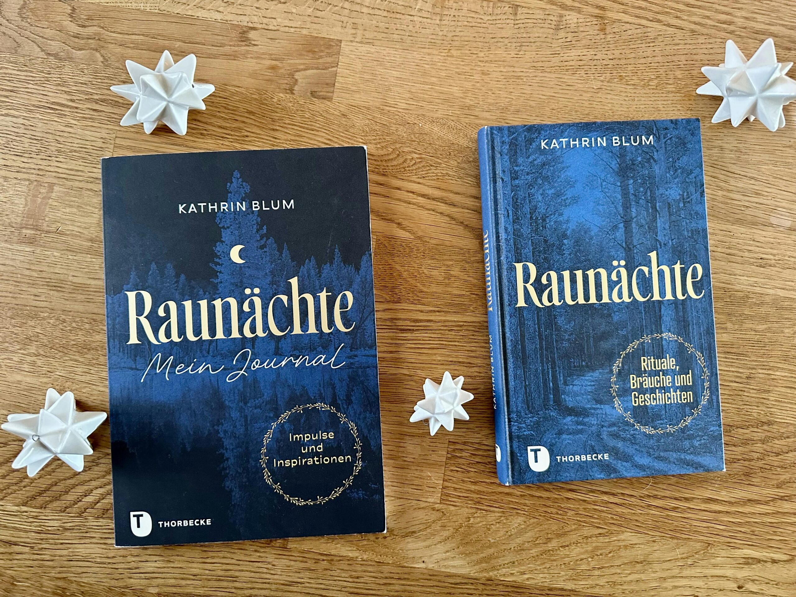 Bücher "Raunächte - Mein Journal" und "Raunächte" von Kathrin Blum auf einem Holztisch. Daneben weiße Porzellan-Sterne.