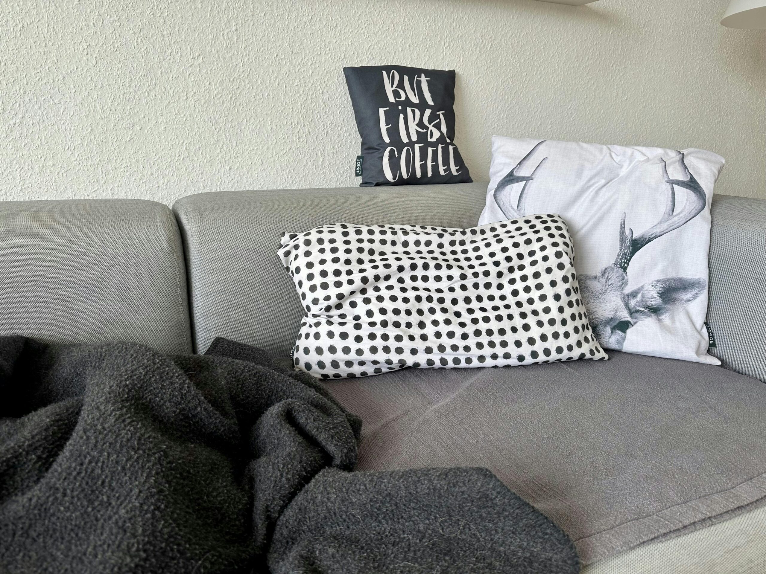 Graue Couch mit schwarz-weißen Kissen und einer dunkelgrauen Wolldecke.
